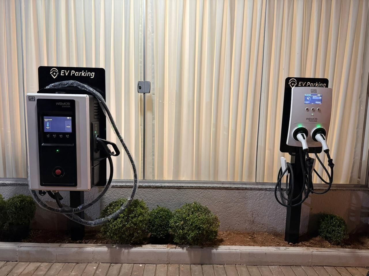 Two EV parking stations with charging cables and control panels, labeled 'EV Parking,' against a corrugated metal wall.
