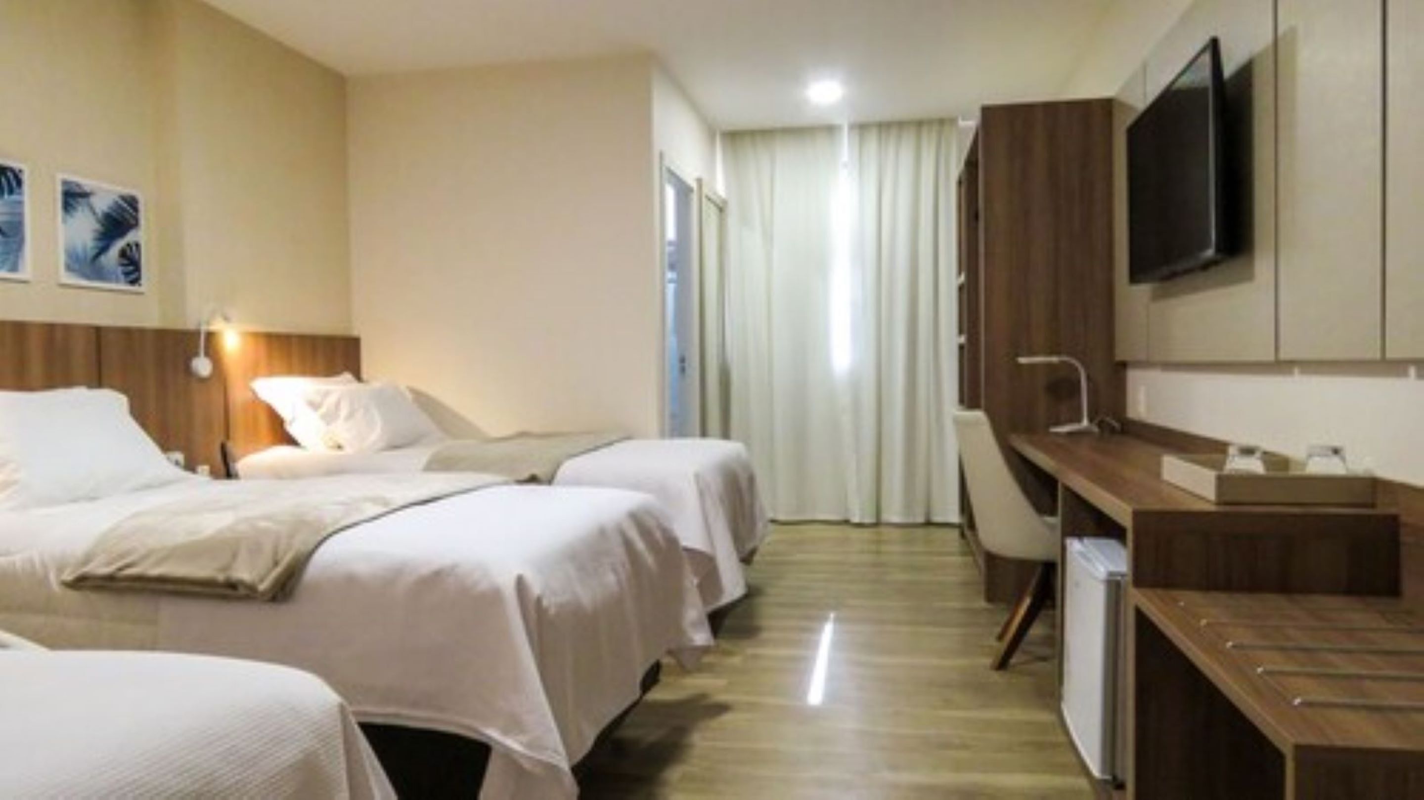 Habitación de hotel con dos camas, un escritorio, un televisor y una ventana con cortinas.