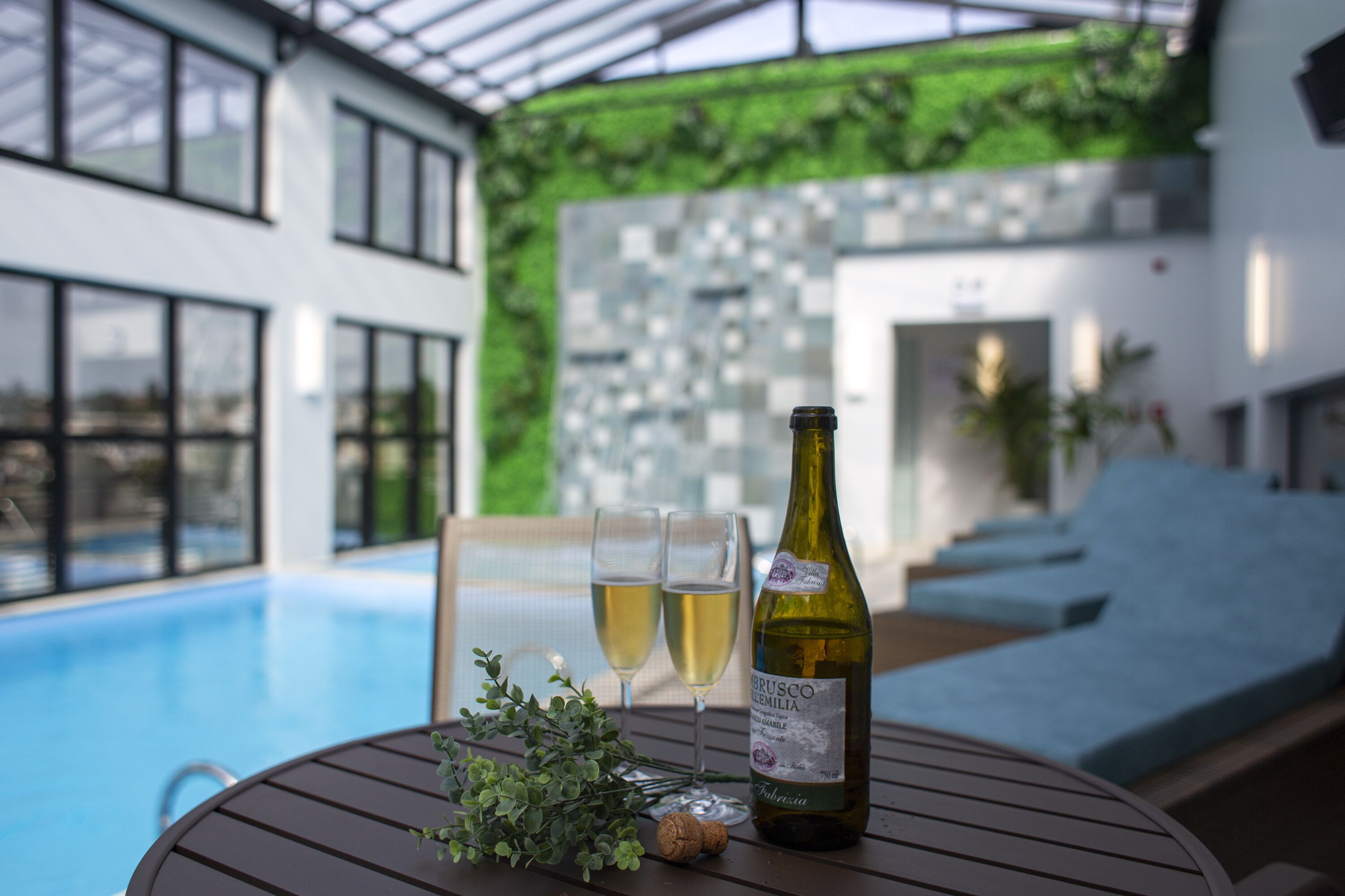 A poolside table with a bottle of wine, two glasses, and a cork.