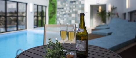 A poolside table with a bottle of wine, two glasses, and a cork.