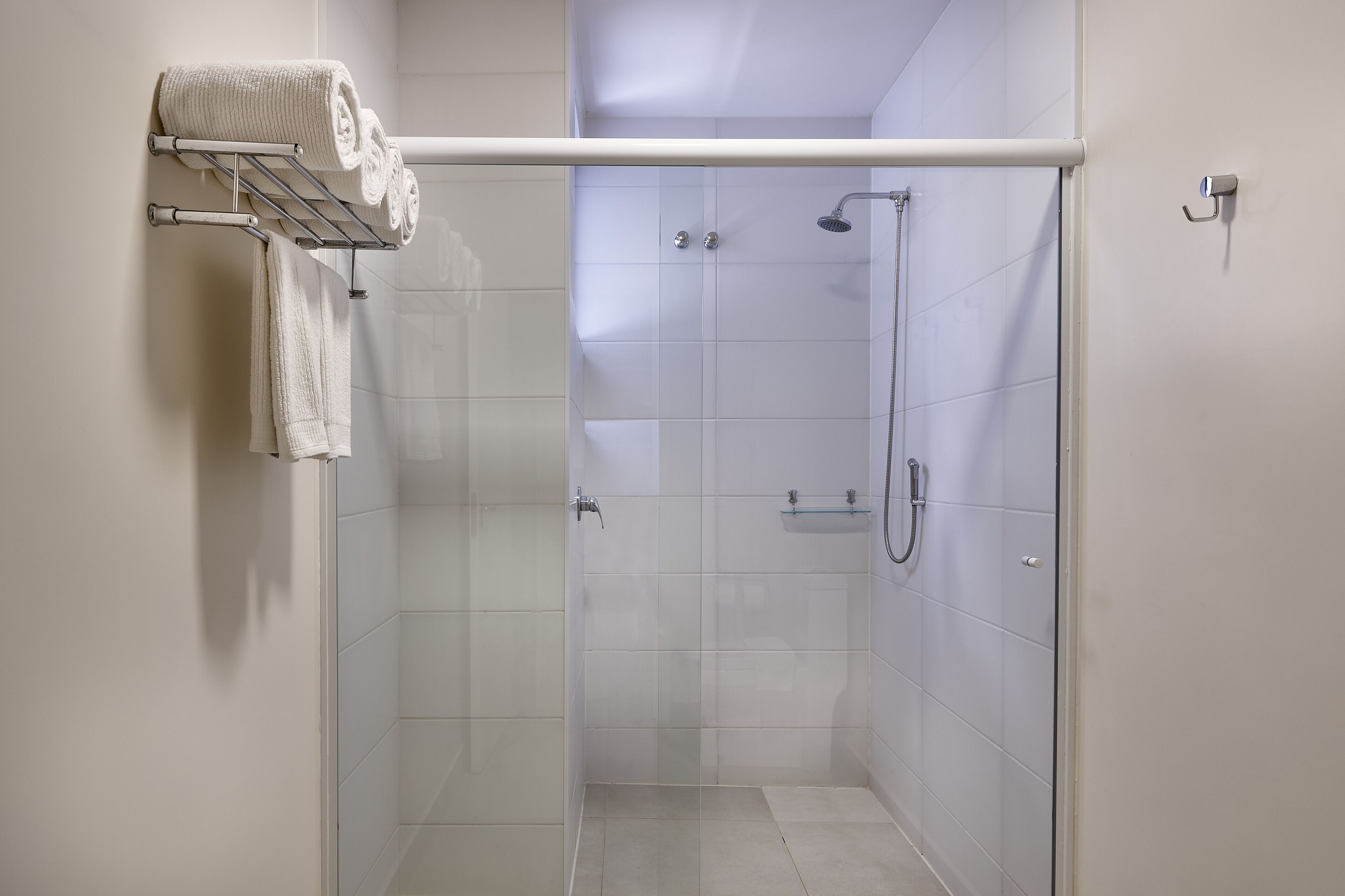 Ein modernes Duschbad mit Glasabtrennung, einem Handtuchhalter mit gefalteten Handtüchern und einer Handbrause.
