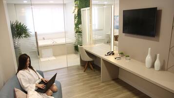 Espaço de escritório moderno com divisória de vidro, uma mesa com computador, uma cadeira e uma TV na parede.