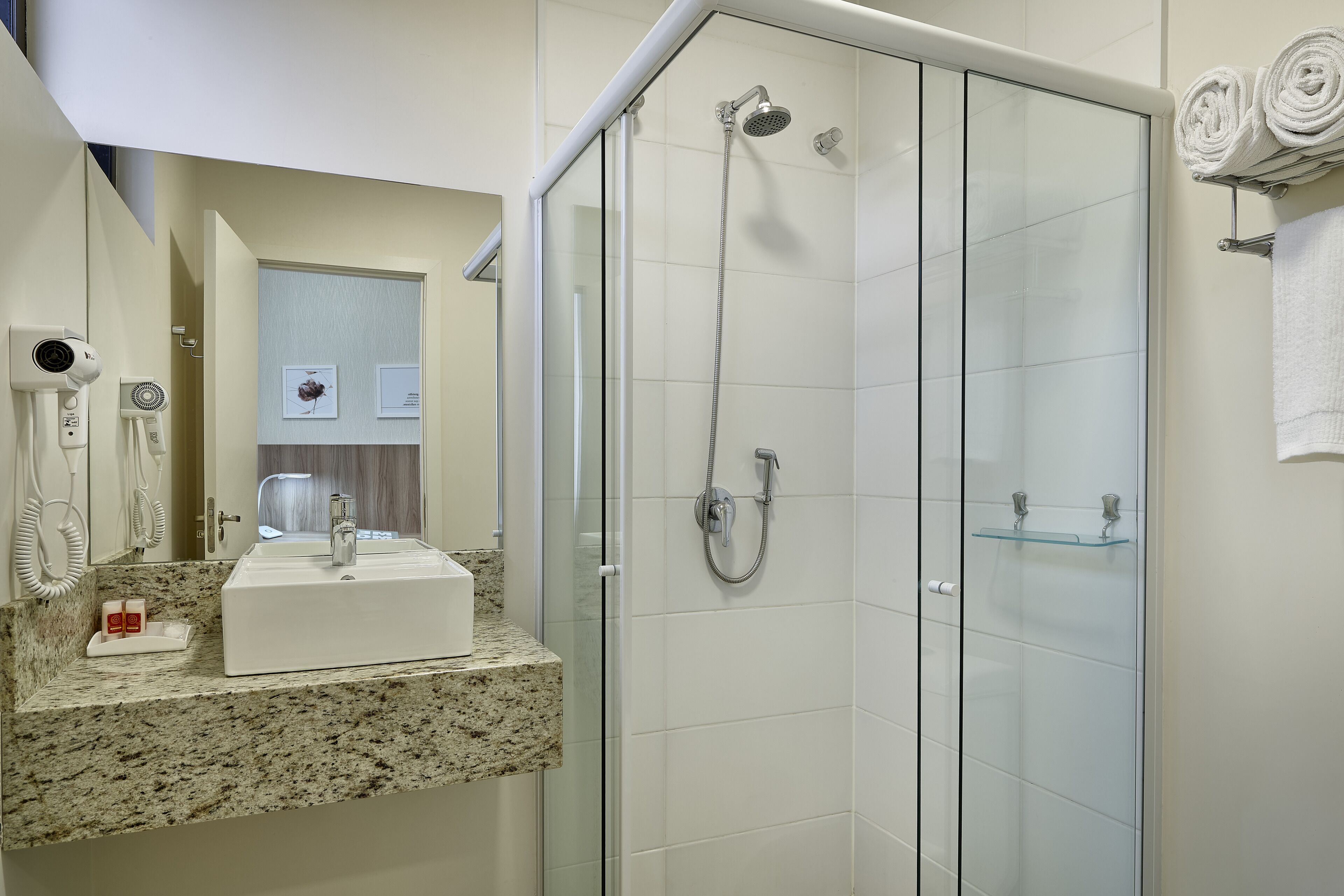 A modern bathroom with a granite countertop, a white sink, a glass shower enclosure, and a towel rack with folded towels.