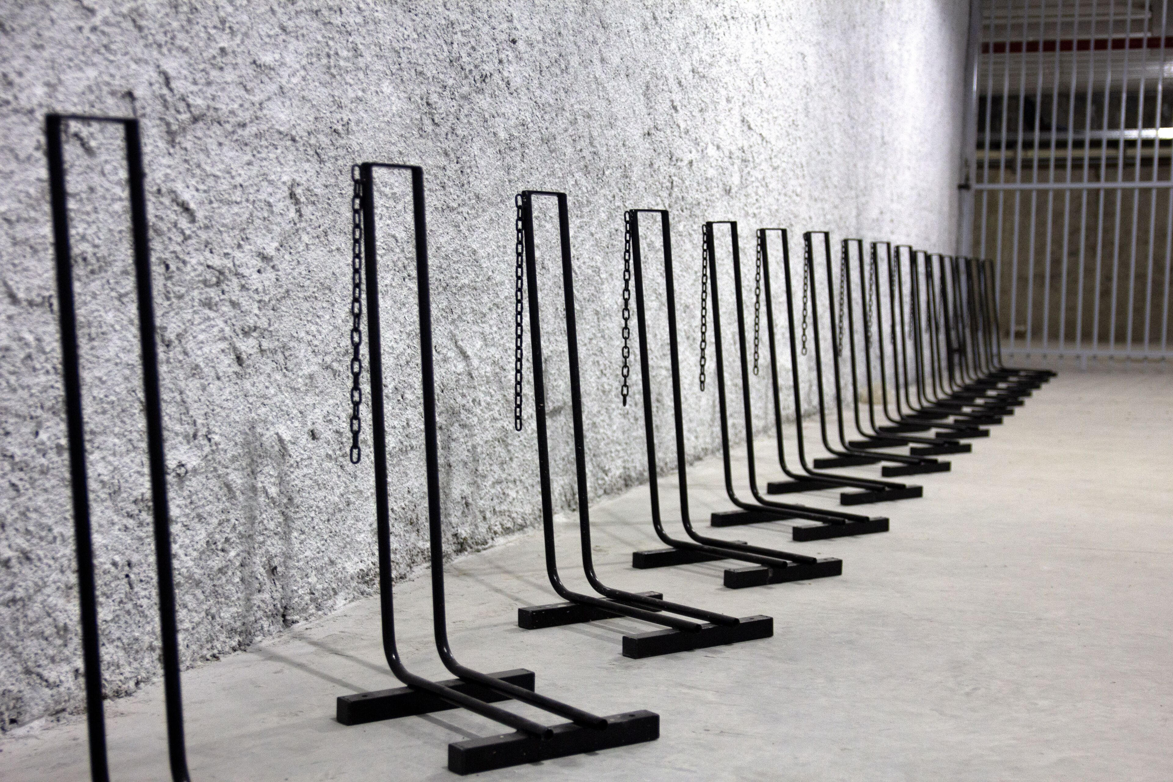 A row of black metal barriers with chains, set against a textured wall, in a hallway with a concrete floor.