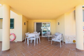 A covered patio with a table and chairs, a sofa, and a pool in the background.
