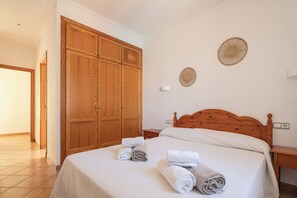 A hotel room with a large wooden wardrobe, a bed with neatly folded towels, a bedside table, and a wall-mounted decorative plate.