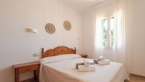 Ein Schlafzimmer mit einem hölzernen Bett, einem Nachttisch, zwei Wandlampen und einem Fenster mit Vorhängen.
