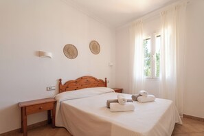 Une chambre à coucher avec un lit en bois, une table de chevet, une commode, deux lampes fixées au mur et une fenêtre avec des rideaux.