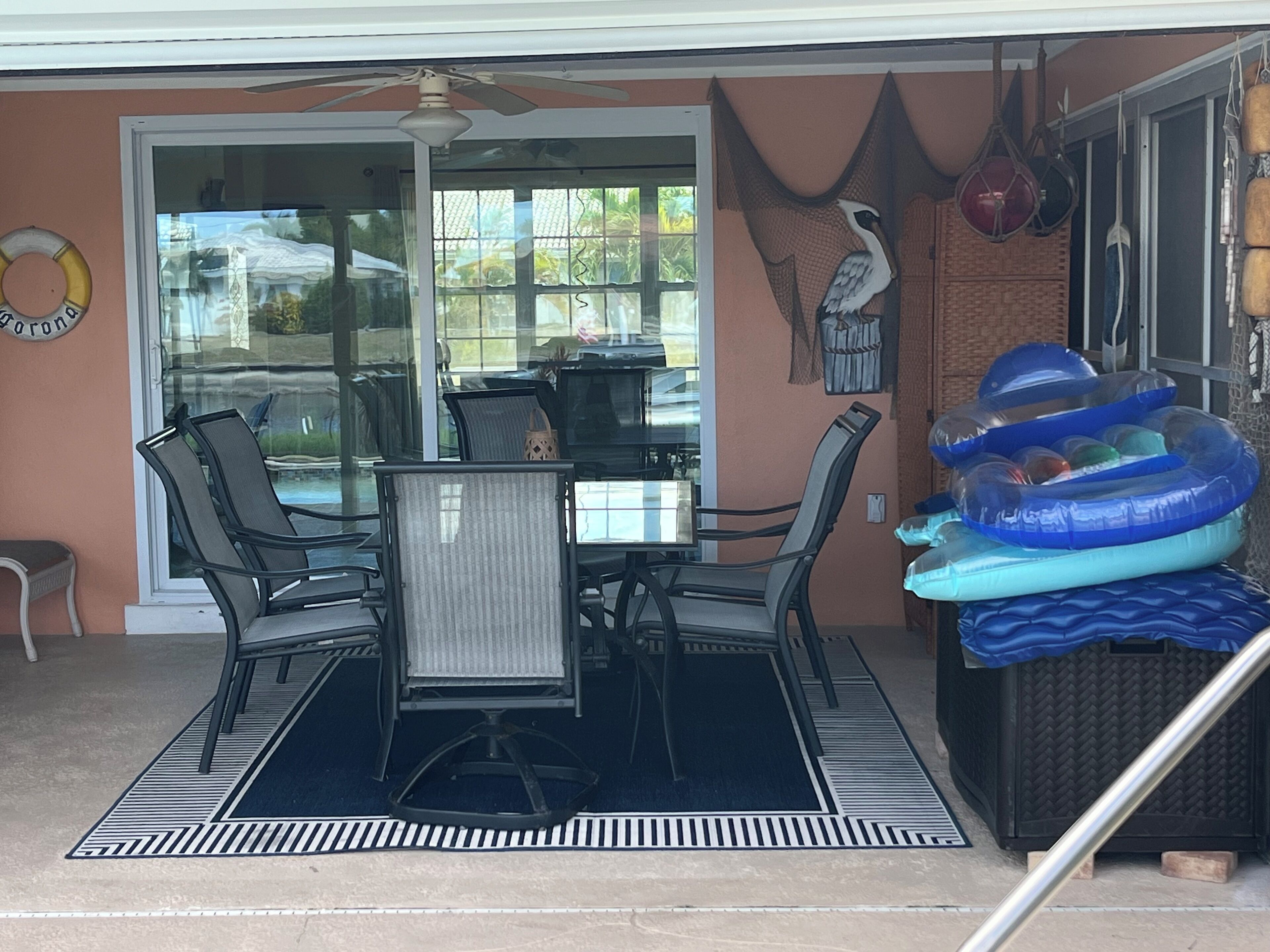 Une terrasse couverte avec une table et des chaises, un ventilateur de plafond et des bouées gonflables.