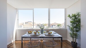 A dining area with a table set for breakfast, large windows, and a potted plant. - Bright & Sunny Beach House (Leça da Palmeira)