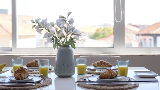 A breakfast table with croissants, juice, and a vase of flowers. - Bright & Sunny Beach House (Leça da Palmeira)
