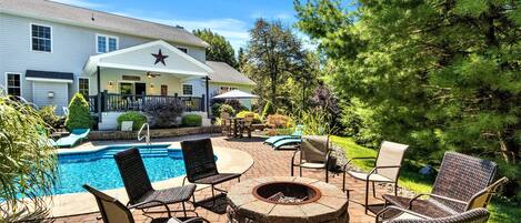 A pool area with lounge chairs, a fire pit, and a house with a star on the roof.