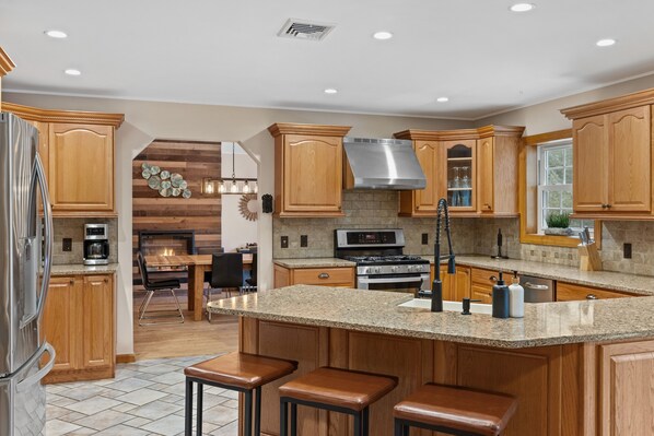 Una cocina moderna con armarios de madera, encimeras de granito, una campana extractora de acero inoxidable y una isla central con taburetes de bar.