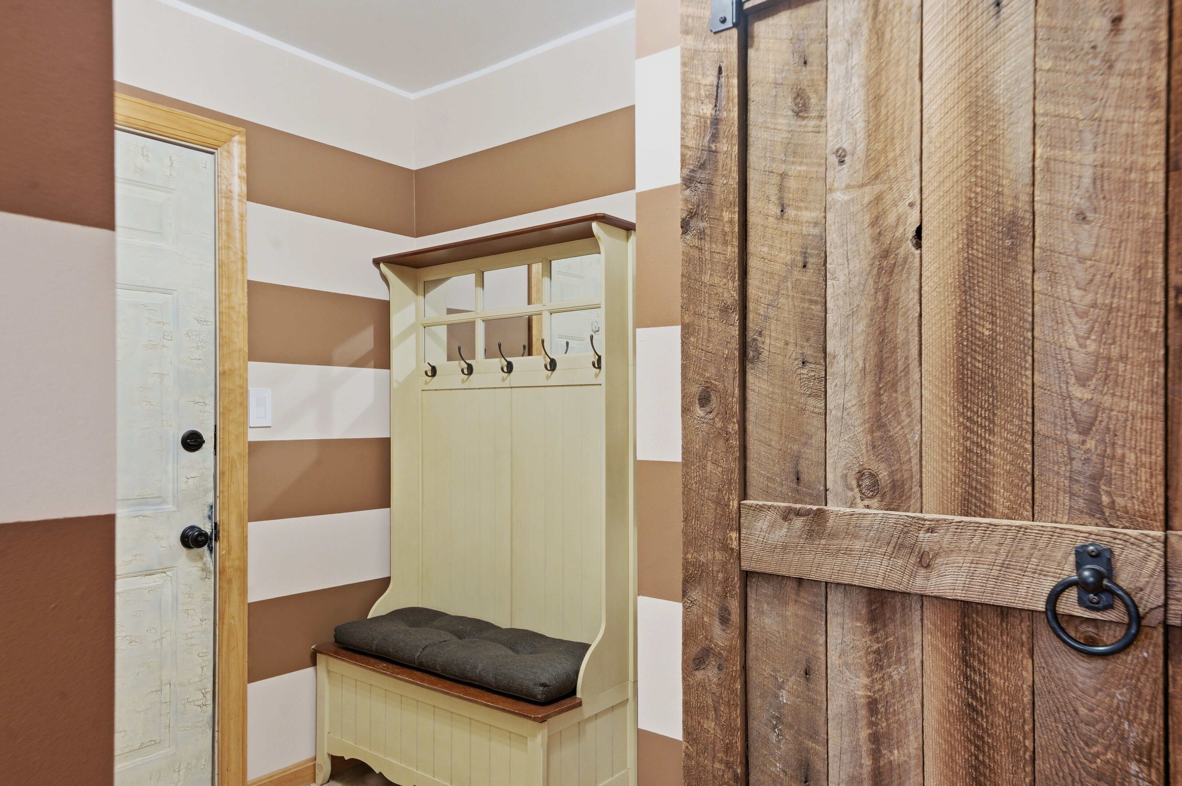 Una habitación con un banco de madera, un perchero y una puerta.