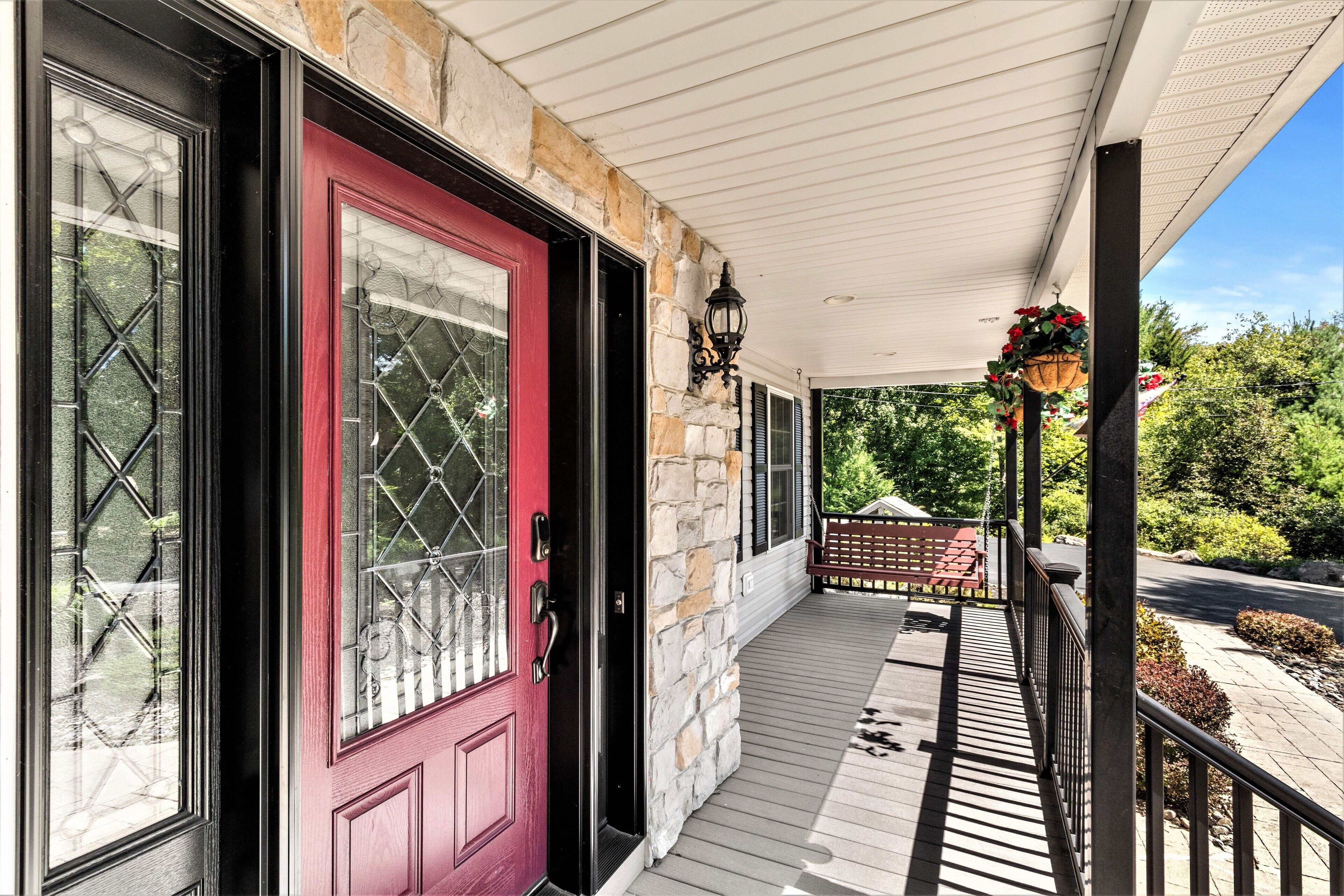 A covered porch with a red door, stone walls, and a hanging flower basket.
