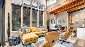 A modern living room with a large window, a yellow sofa, and a wooden ceiling.
