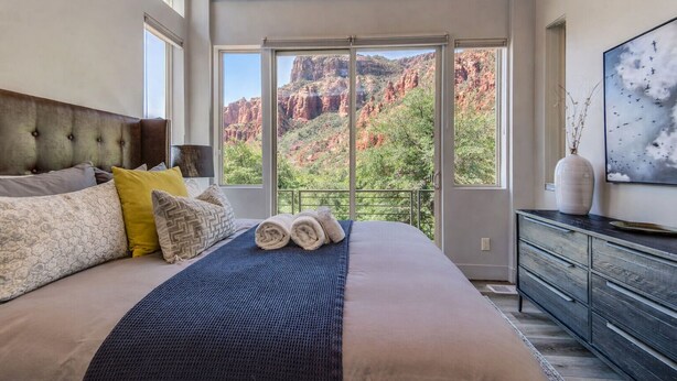 A bedroom with a large bed, a view of red rock formations, and a modern dresser.