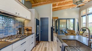 A modern kitchen with a wooden ceiling, a built-in stove, and a large window overlooking a scenic view.