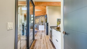 A modern kitchen with a wooden ceiling, a central island, and a view into the dining area.