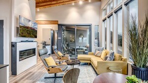 A modern living room with a fireplace, comfortable seating, and large windows.