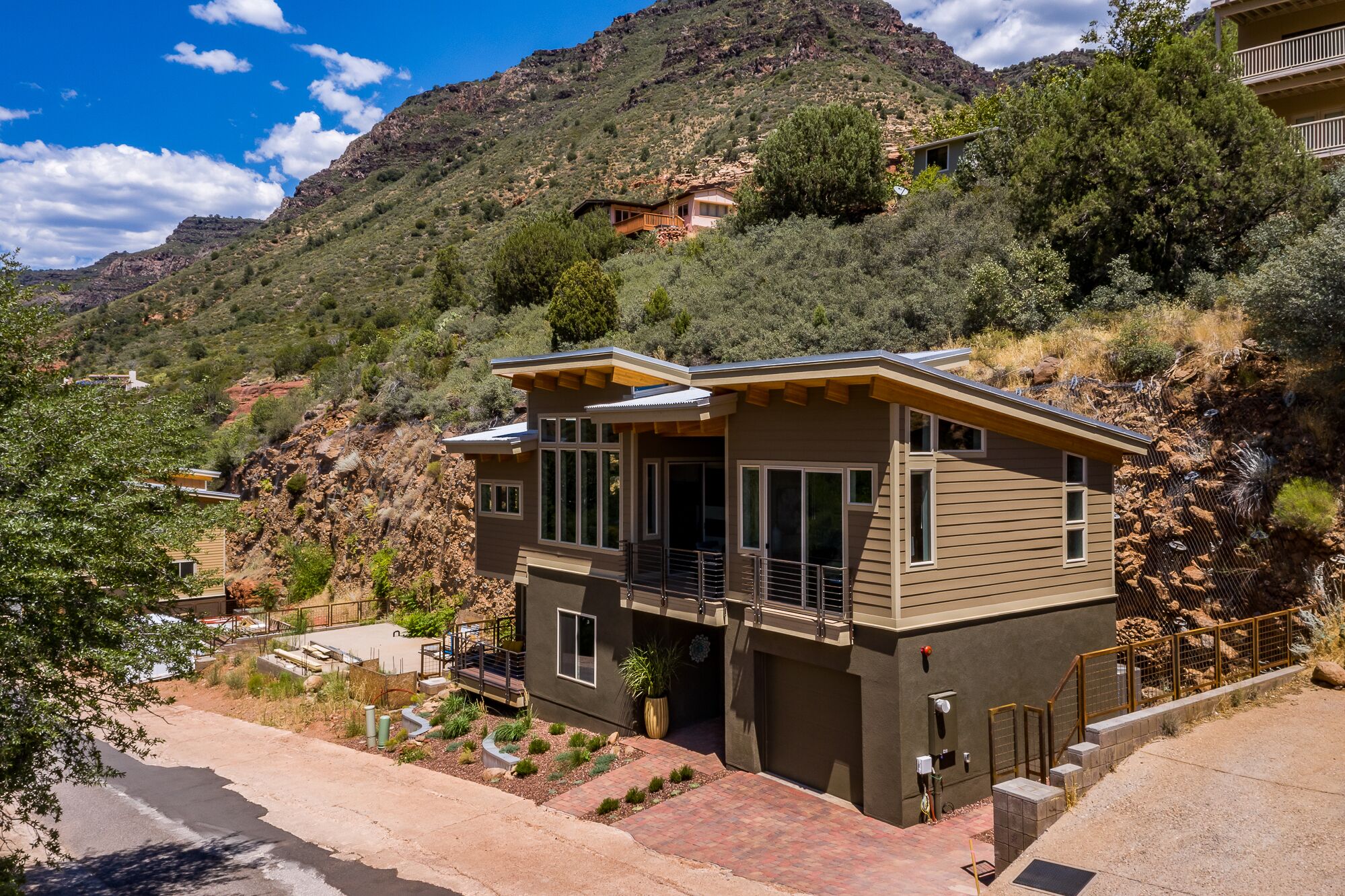 A modern two-story house with a balcony, situated on a hillside with a mountain backdrop.