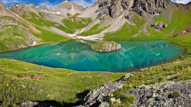 A mountain landscape with a clear turquoise lake surrounded by rocky terrain and green vegetation.