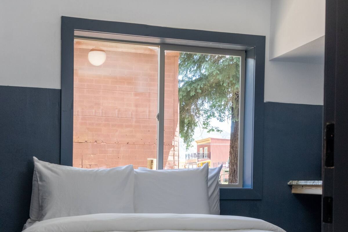 A bedroom with a bed, a window, and a view of a brick building outside.