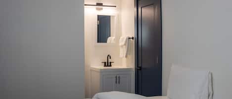 A bedroom with a bed, a nightstand, a mirror, a sink, and a door.