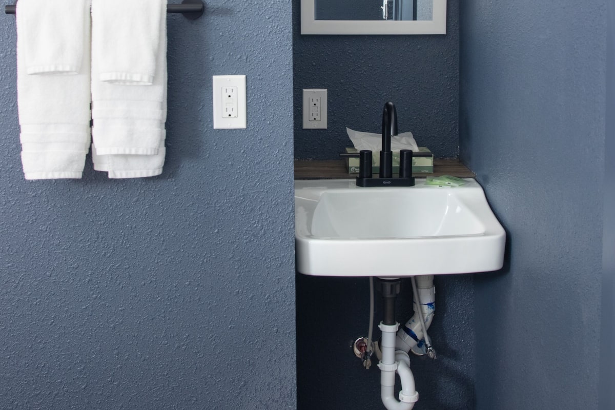 A bathroom with a white sink, a mirror, and a microwave on a shelf.
