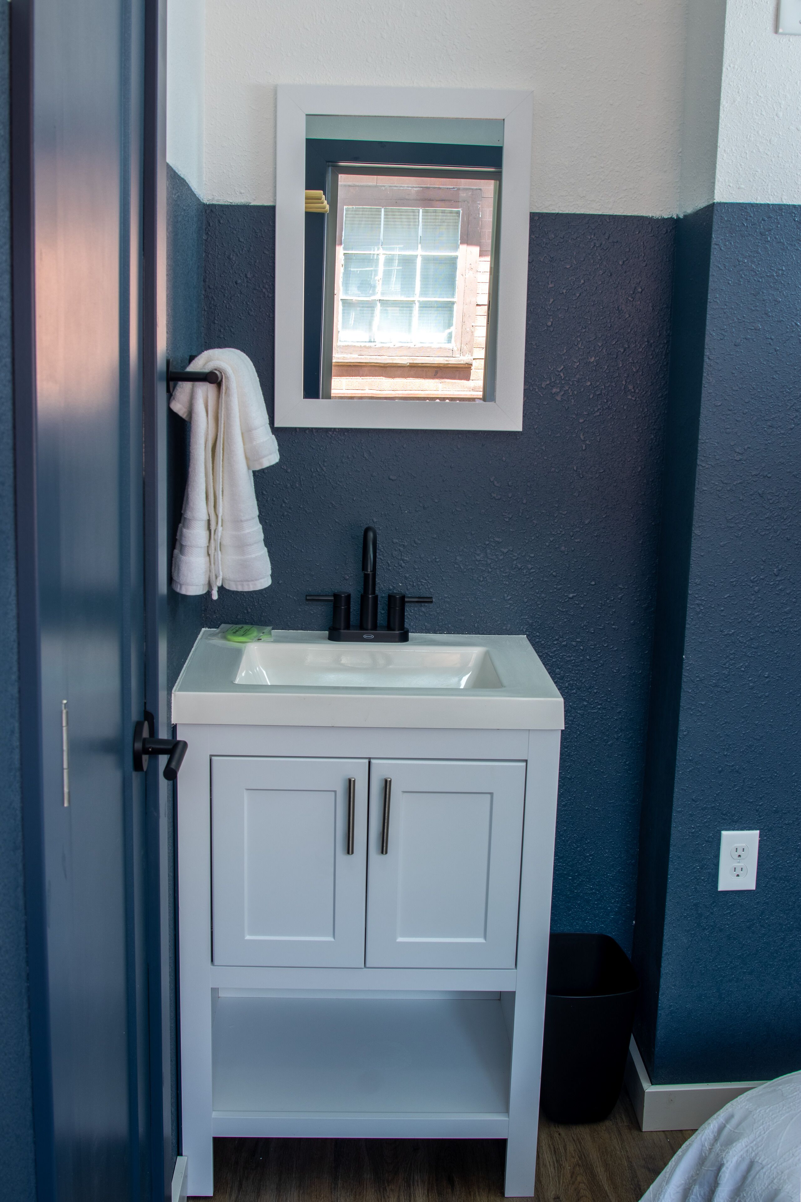 A bathroom with a white vanity, a window above the sink, and a towel rack.