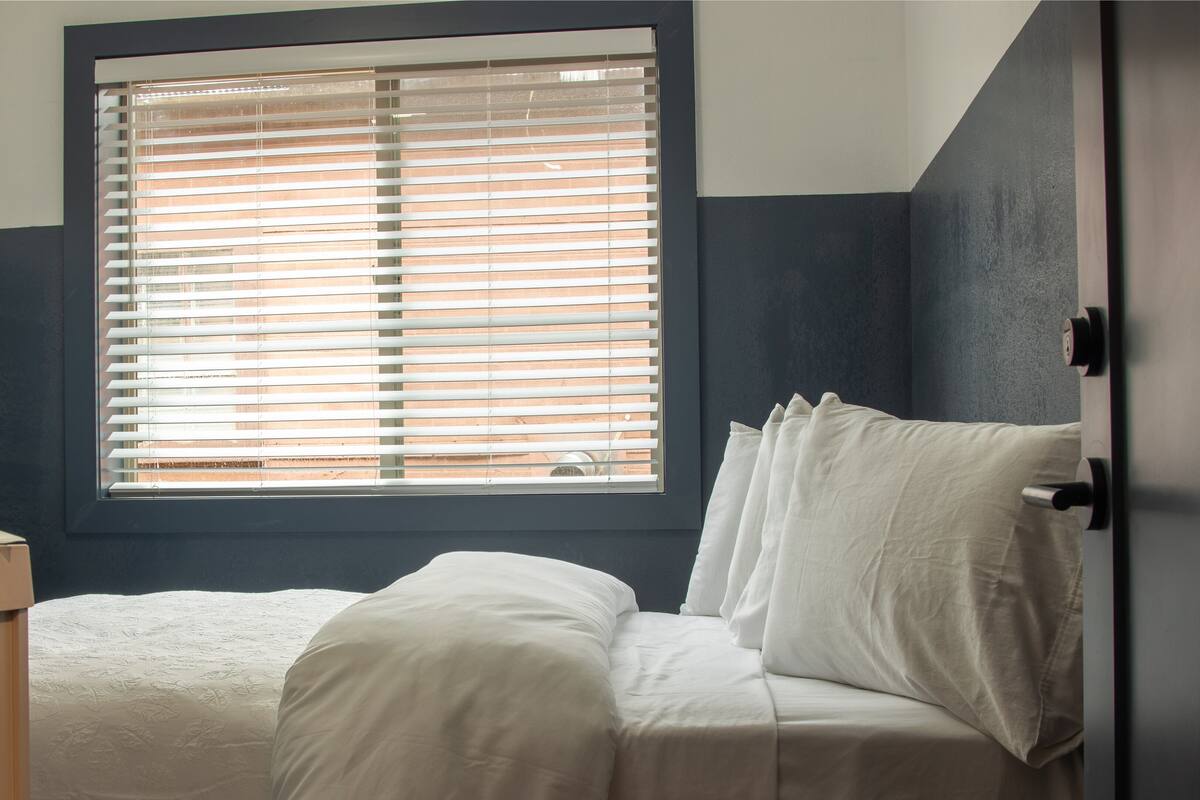 A bedroom with a bed, a window with blinds, and a door.