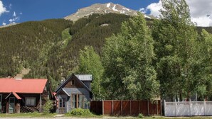 A cabin with a red roof and a wooden exterior, surrounded by a fenced area and a mountain in the background.