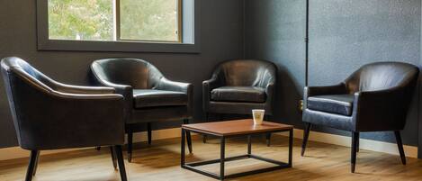 Een kamer met drie leren fauteuils, een houten salontafel en een raam met uitzicht op groen.