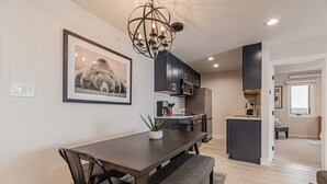 A modern kitchen with dark cabinets, a dining table with chairs, and a chandelier. - Stylish Ski-In/Ski-Out Condo with Sunset Views and Slope Access/Sleeps 5! (Steamboat Springs)
