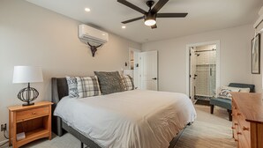 A bedroom with a bed, bedside table, lamp, ceiling fan, air conditioning unit, and a door leading to a bathroom. - Stylish Ski-In/Ski-Out Condo with Sunset Views and Slope Access/Sleeps 5! (Steamboat Springs)