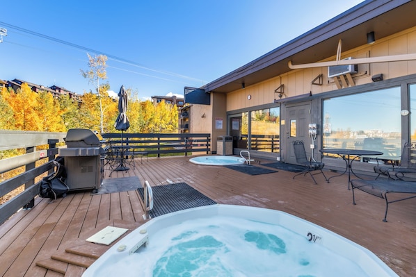 A deck with hot tubs, outdoor seating, and a grill.