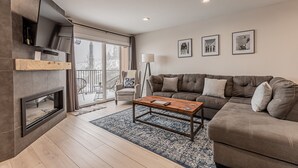 A modern living room with a fireplace, a sofa, a coffee table, and a large window. - Stylish Ski-In/Ski-Out Condo with Sunset Views and Slope Access/Sleeps 5! (Steamboat Springs)