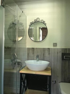 A bathroom with a glass shower enclosure, a white sink with a wooden countertop, and a round mirror with a decorative frame. - La Casa Carina (Antalya)