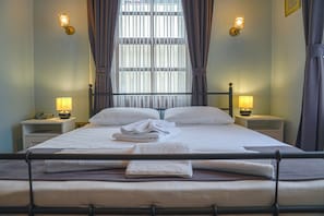 A neatly made bed with white linens and towels, two bedside lamps, and a window with curtains. - La Casa Carina (Antalya)