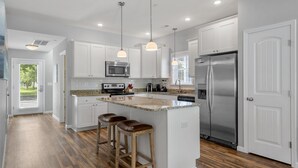 A modern kitchen with white cabinets, stainless steel appliances, and a wooden island with bar stools. - The E Gull Has Landed: Private Spa, Shared Pool (Kill Devil Hills)