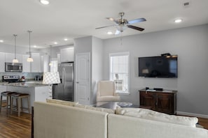 A modern kitchen with a central island, bar stools, a ceiling fan, and a TV mounted on the wall. - The E Gull Has Landed: Private Spa, Shared Pool (Kill Devil Hills)
