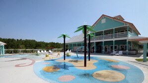 A pool area with a colorful play zone, lounge chairs, and a building with a balcony. - The E Gull Has Landed: Private Spa, Shared Pool (Kill Devil Hills)
