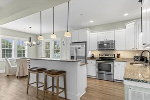 A modern kitchen with white cabinets, stainless steel appliances, and a granite countertop. - Bay Breeze: Shared Pool, Hot Tub, Short Stays OK (Kill Devil Hills)