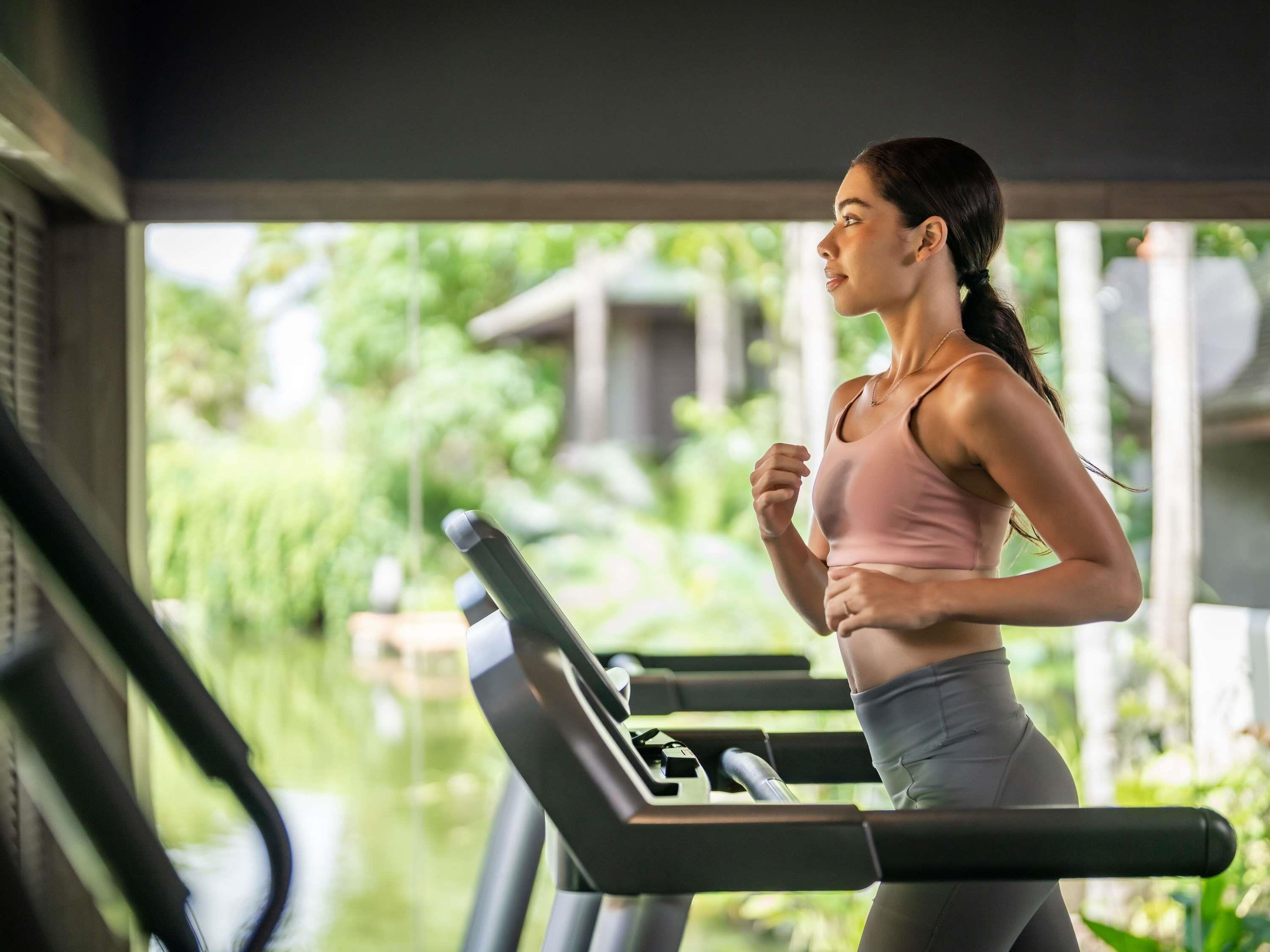 Una persona corre en una cinta de correr con vista a la vegetación exterior.