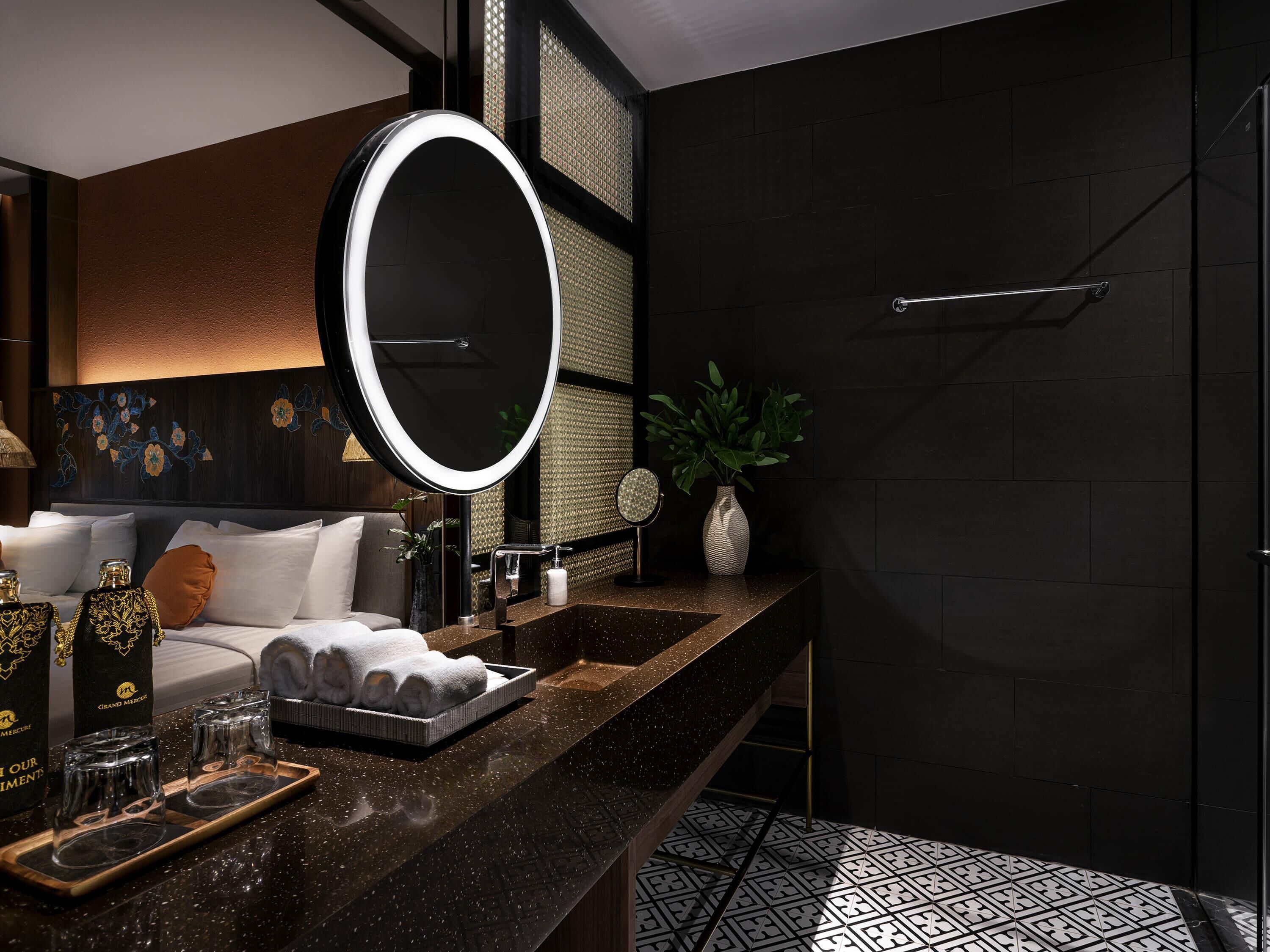 A modern bathroom with a large mirror, a black countertop, and a shower area.