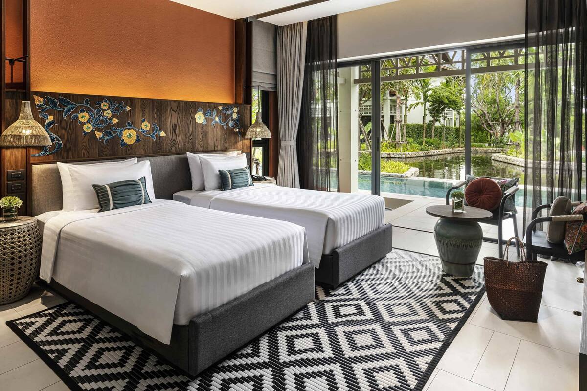 Habitación de hotel con dos camas, un ventanal con vista a una piscina, un tapete tejido y un panel decorativo en la pared.