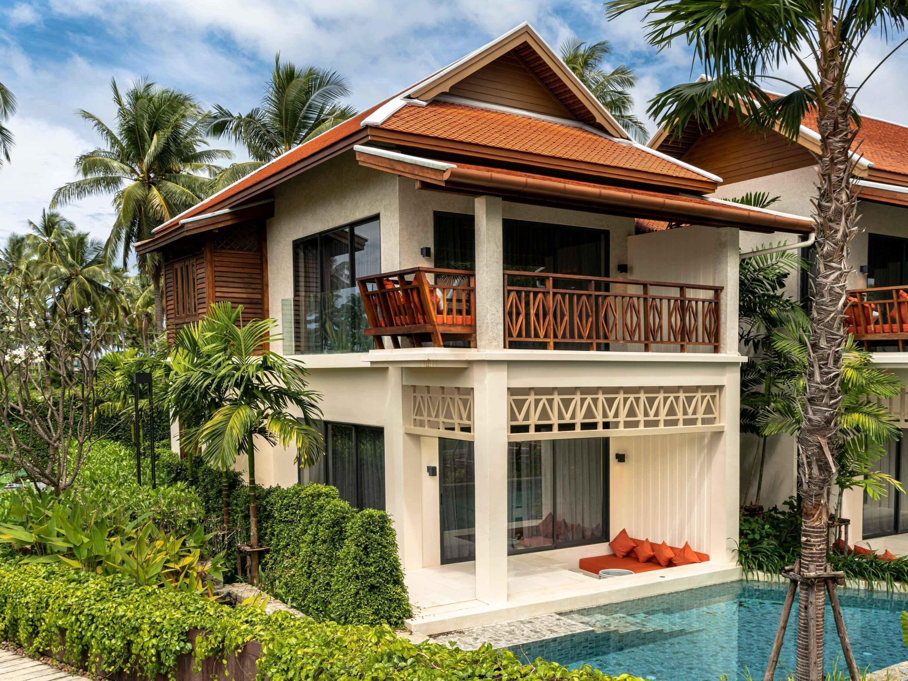 A two-story resort with a pool, surrounded by lush greenery and palm trees.