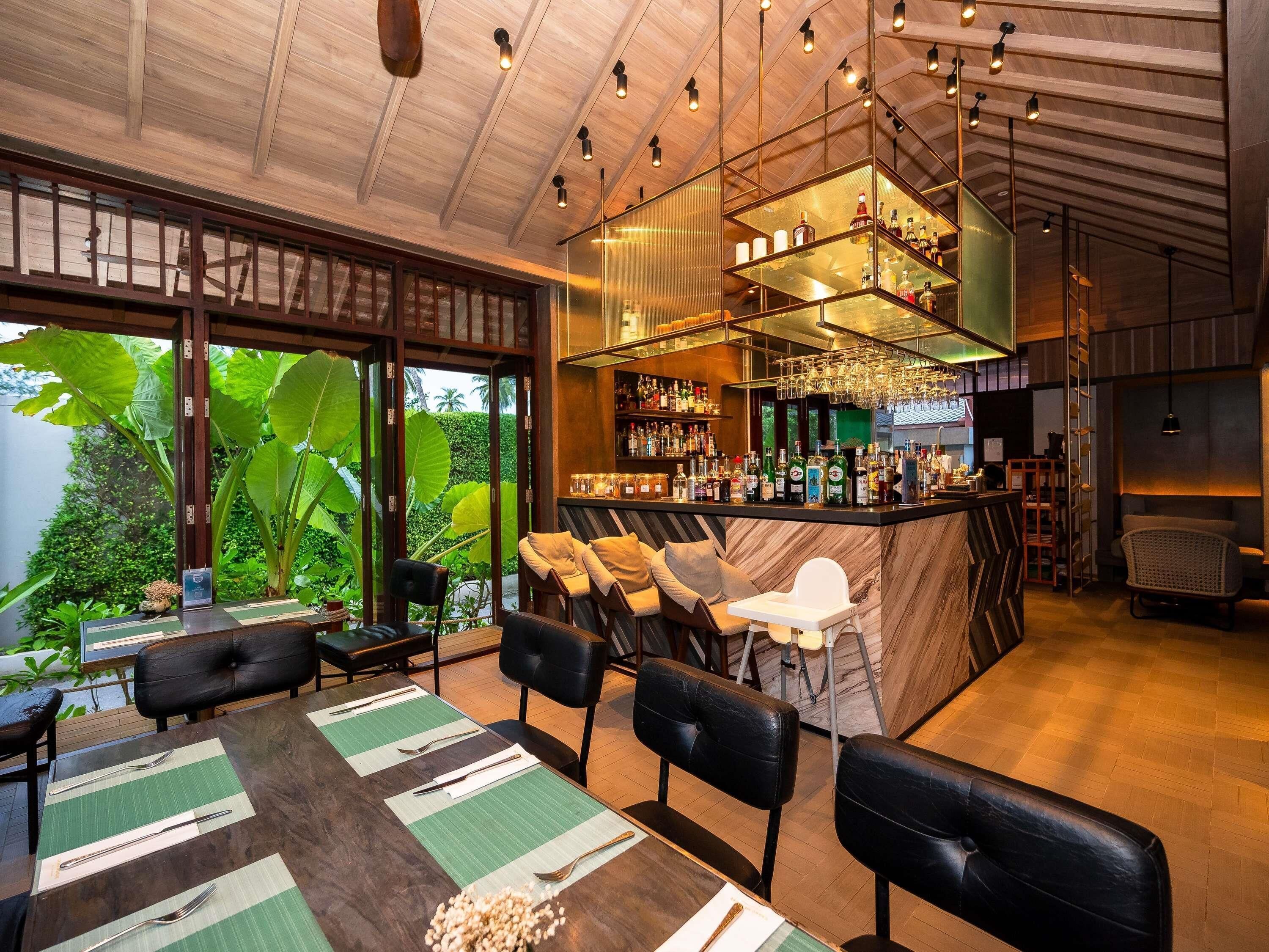 Un restaurante con barra, mesas de comedor con sillas y vistas a zonas verdes.