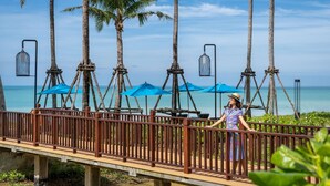 A wooden bridge with railings, palm trees, and blue umbrellas. - Grand Mercure Khao Lak Bangsak (Takua Pa)