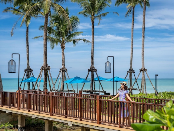 A wooden bridge with railings, palm trees, and blue umbrellas. - Grand Mercure Khao Lak Bangsak (Takua Pa)